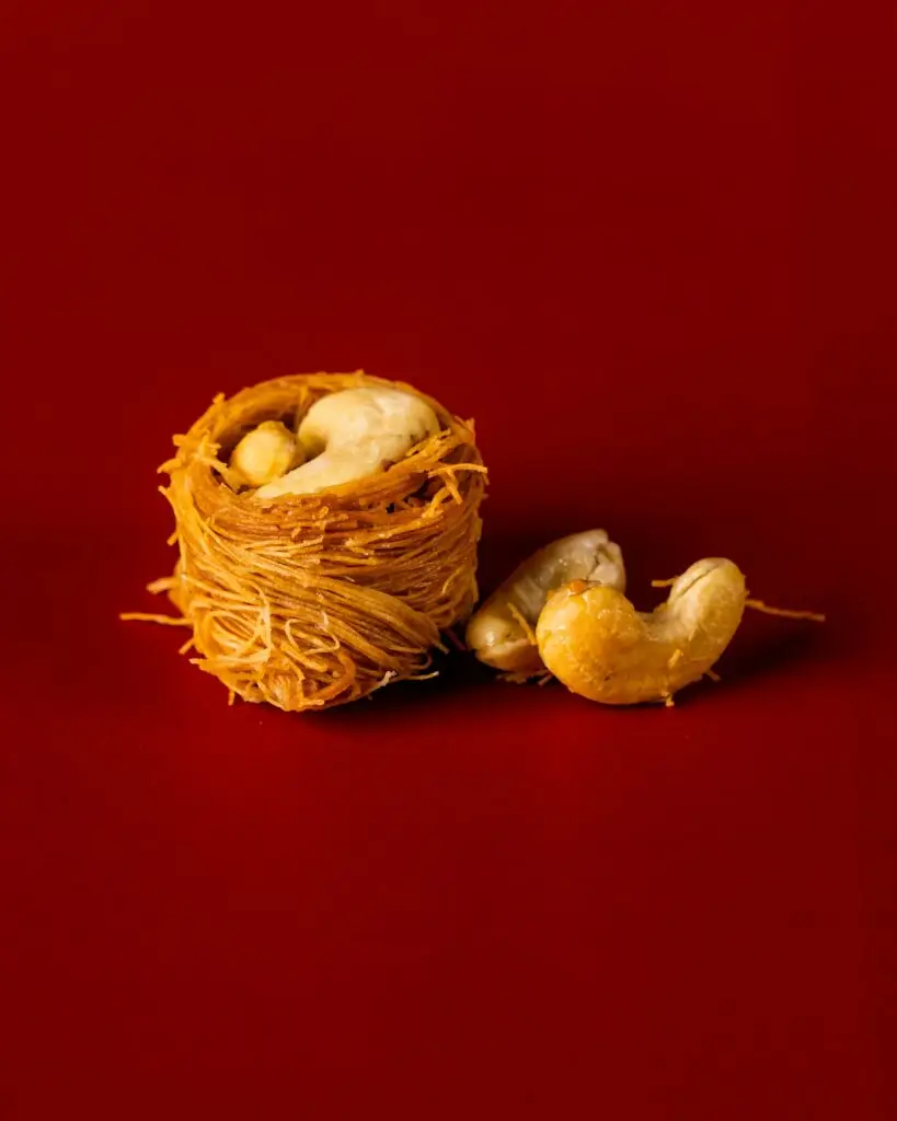 Enticing kadayif baklava with cashew nuts on a vibrant red backdrop, epitomizing Turkish desserts.